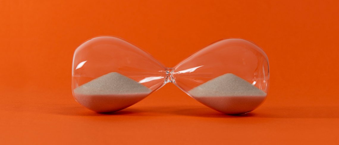 An hourglass tipped on its side in front of a bright orange backdrop.