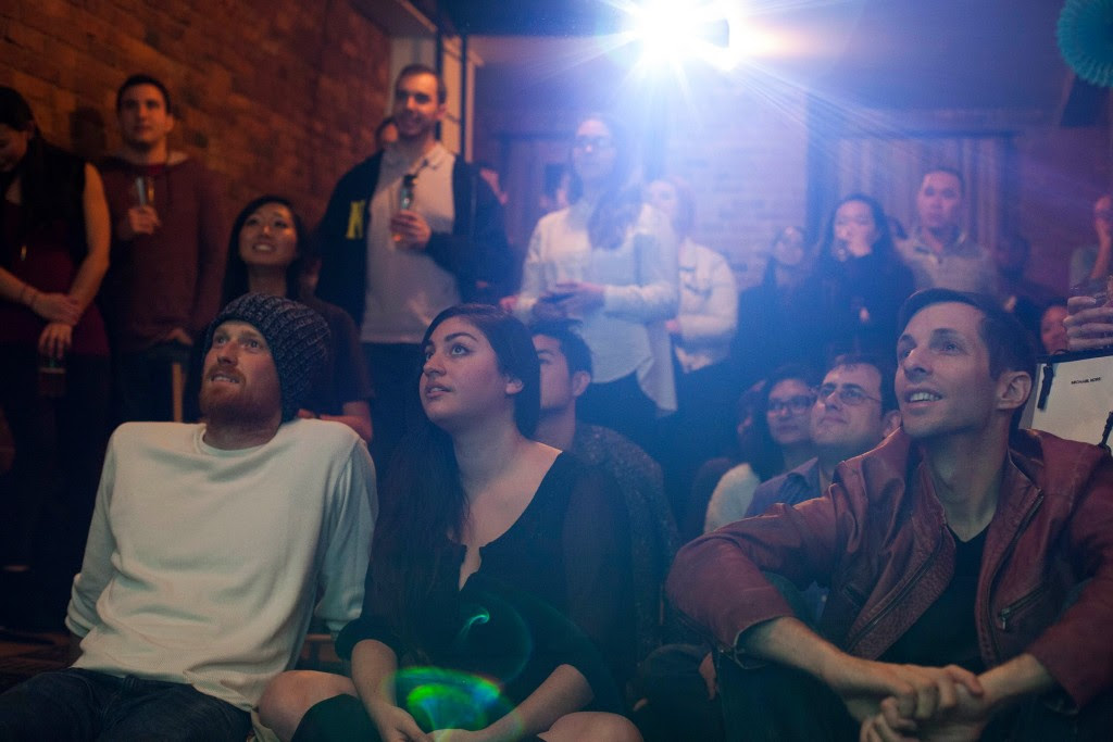 a large group of people in a dark room watching a projected screen off-frame